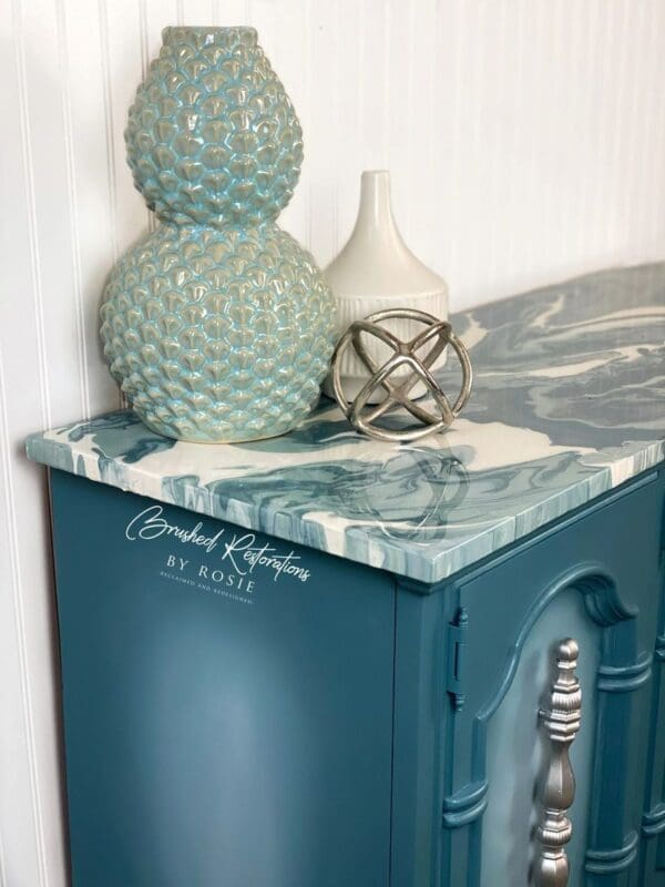 A blue cabinet with paint pour marble top and two vases on top.