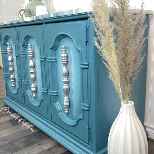 A blue cabinet with silver accents and a white vase.