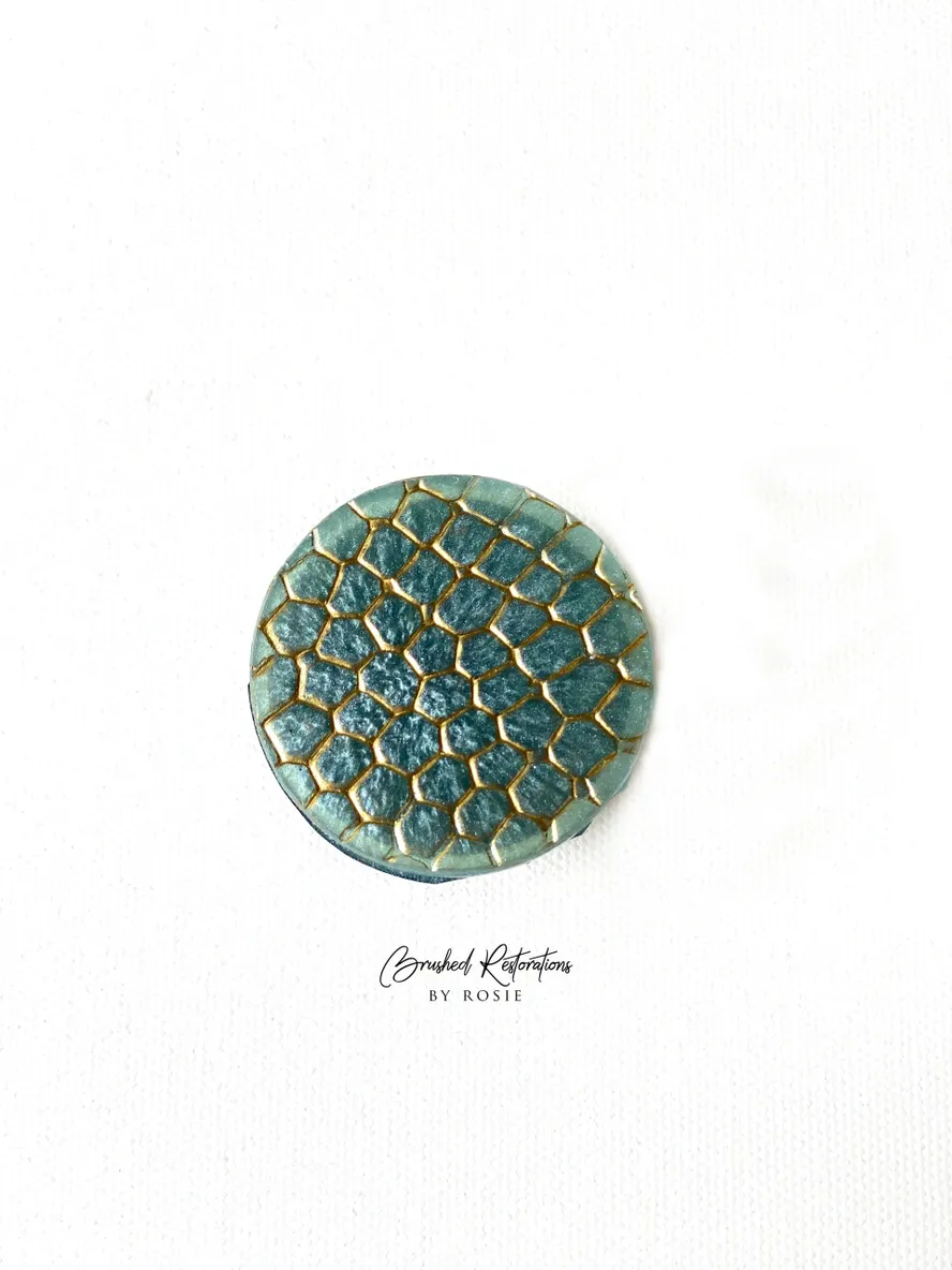 A green and gold round button with the words " stardust collection by paula."