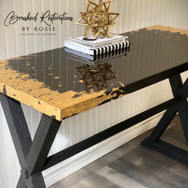 Stylish black and gold epoxy resin tabletop featuring a glossy finish and gold leaf edges, adorned with a modern geometric star sculpture and Chanel-themed books.