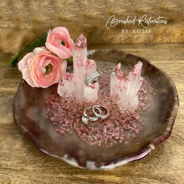 A resin dish with pink flowers and two rings on it.