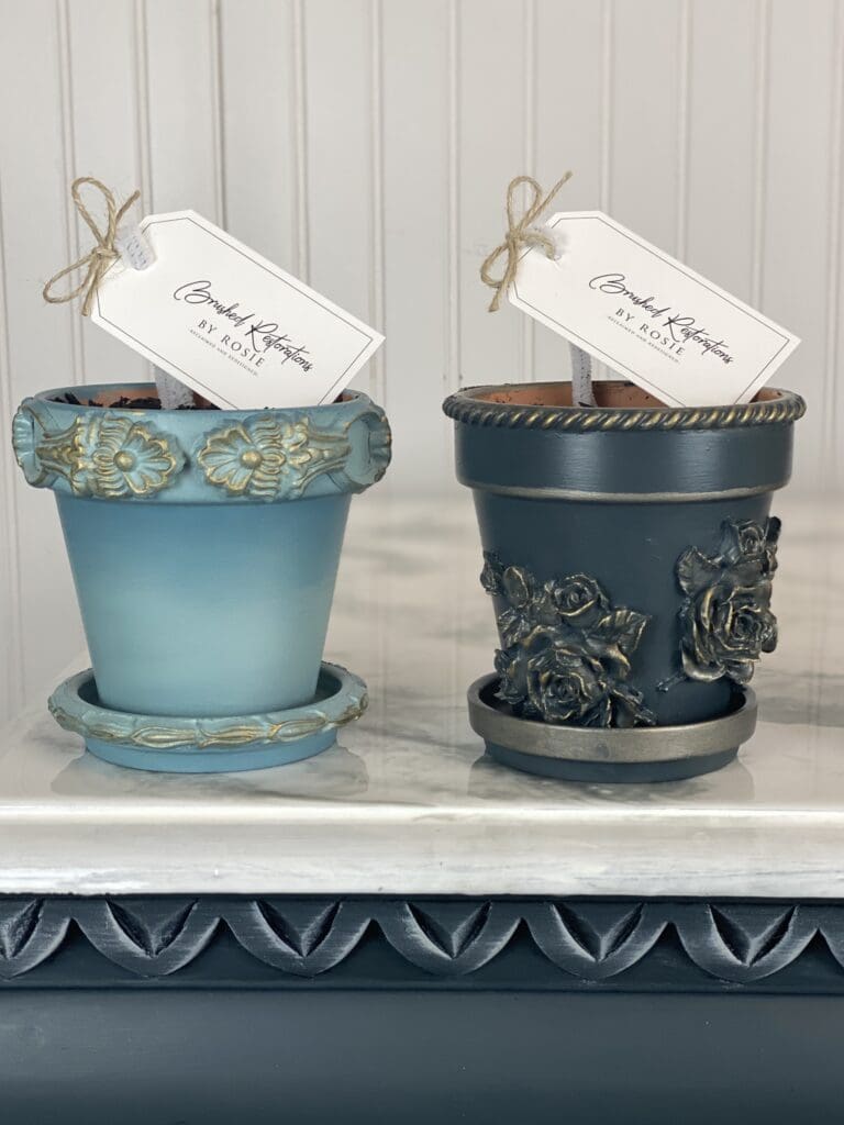 Two intricately designed flower pots in soft blue and deep navy, each adorned with floral motifs and bearing a Brushed Restorations by Rosie tag.