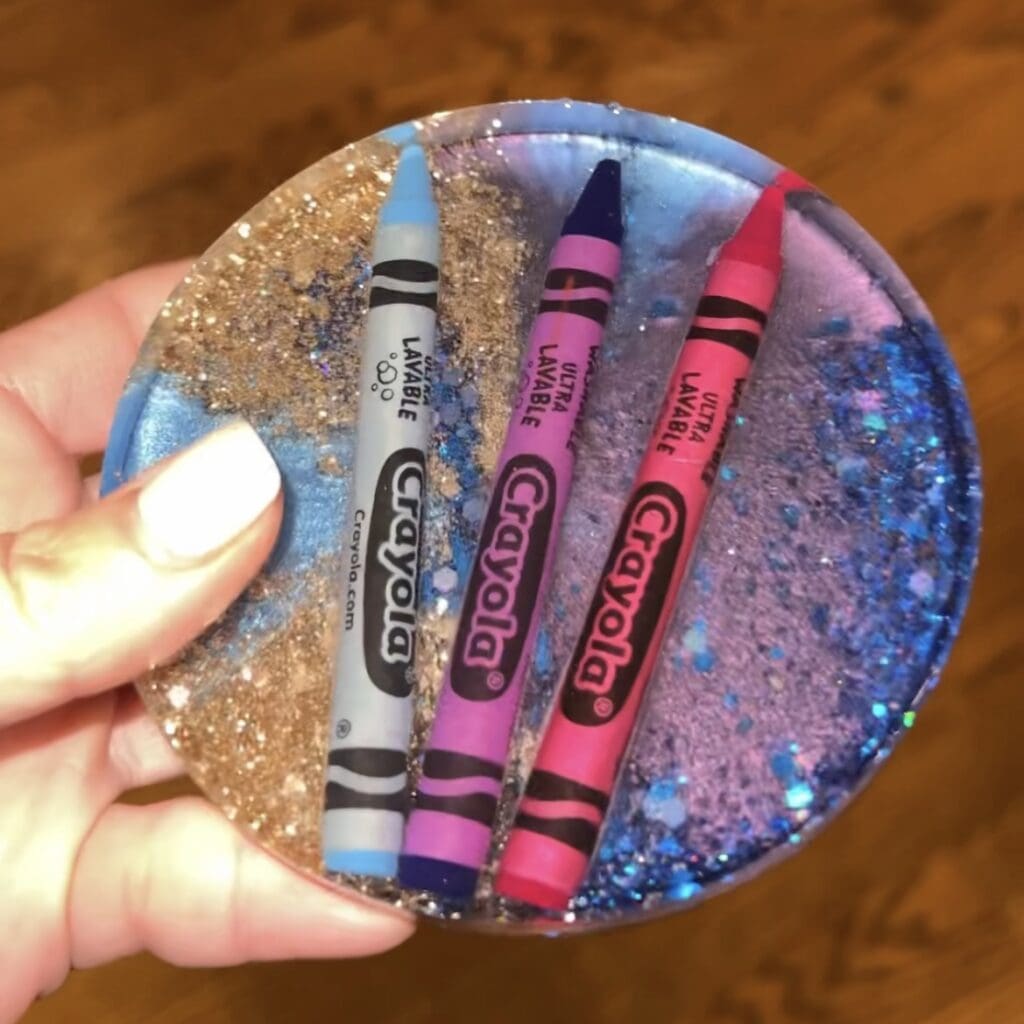 Blue round resin DIY crayon coaster with crayons on the inside and glitter.