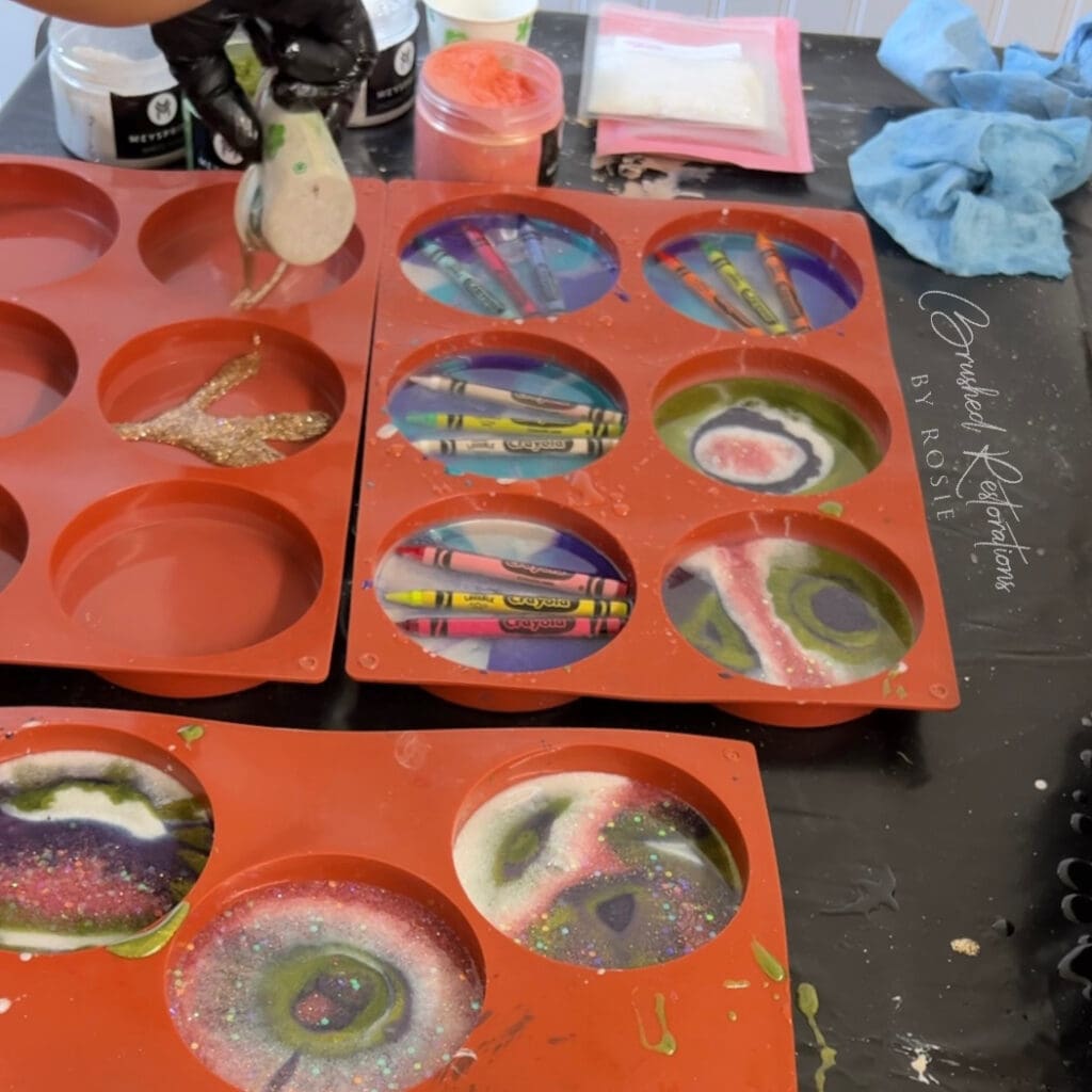 Close-up of adding glitter and pigments to resin-filled molds with crayons, illustrating the crafting process of resin DIY crayon coasters with a focus on adding decorative elements.
