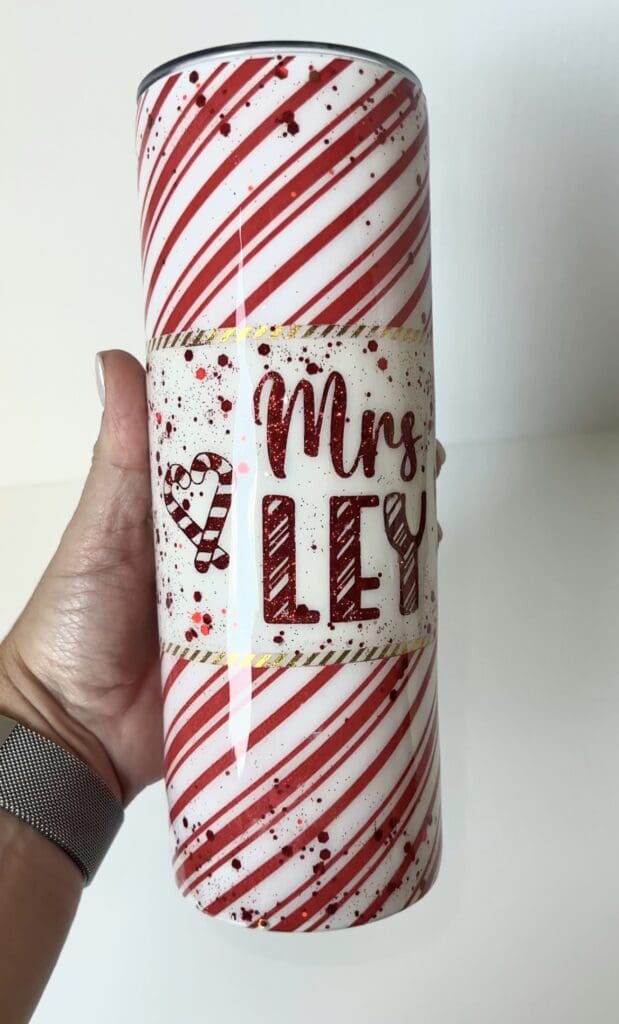 Handheld personalized red and white striped tumbler with "Mrs Ley" text in glitter, ideal for teacher appreciation gifts.