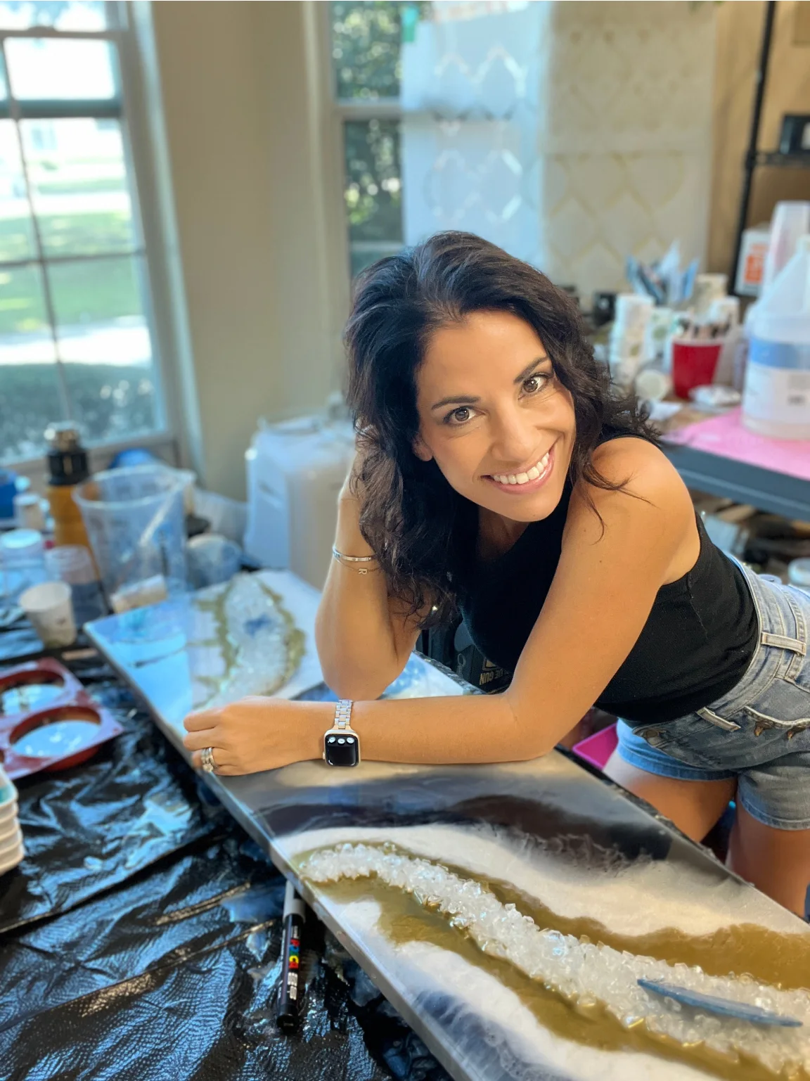 A resin artist leaning on a table over her artwork.