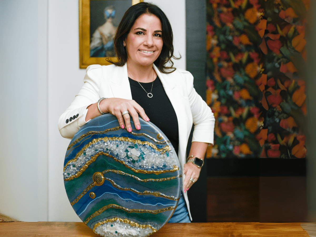 Smiling artist in a white blazer showcasing an exquisite geode resin art piece, symbolizing the blend of creativity and business acumen in resin artistry