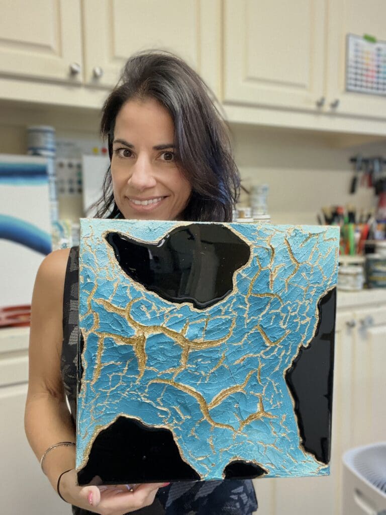 Artist Rosie holding a finished mixed media canvas featuring bold crackle textures and gold leaf detailing.