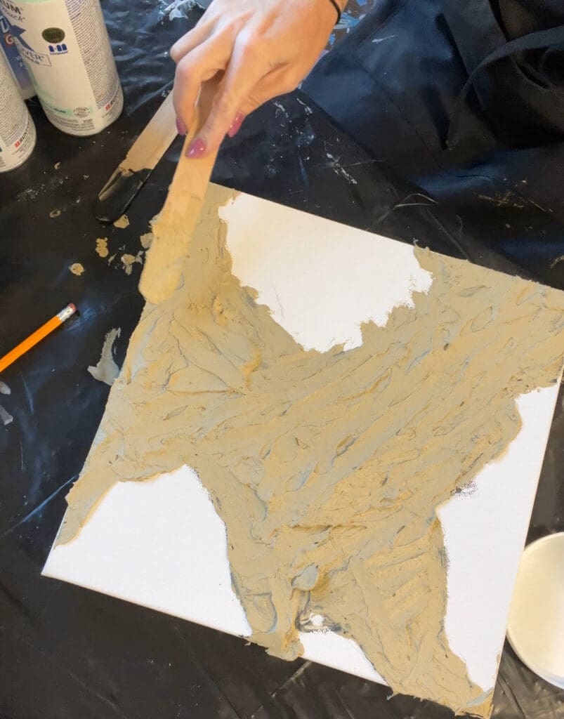 Artist preparing a mixed media canvas with a thick layer of texture medium for a sculptural effect.