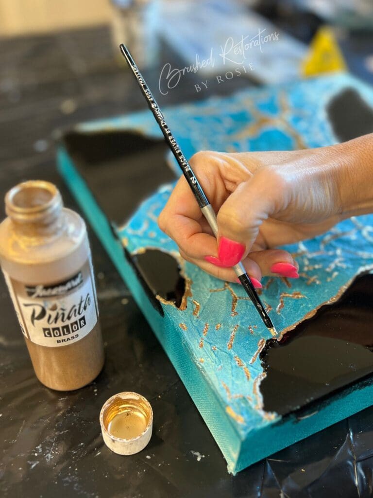 Artist applying gold leaf to a textured mixed media canvas with vibrant turquoise crackle paint.