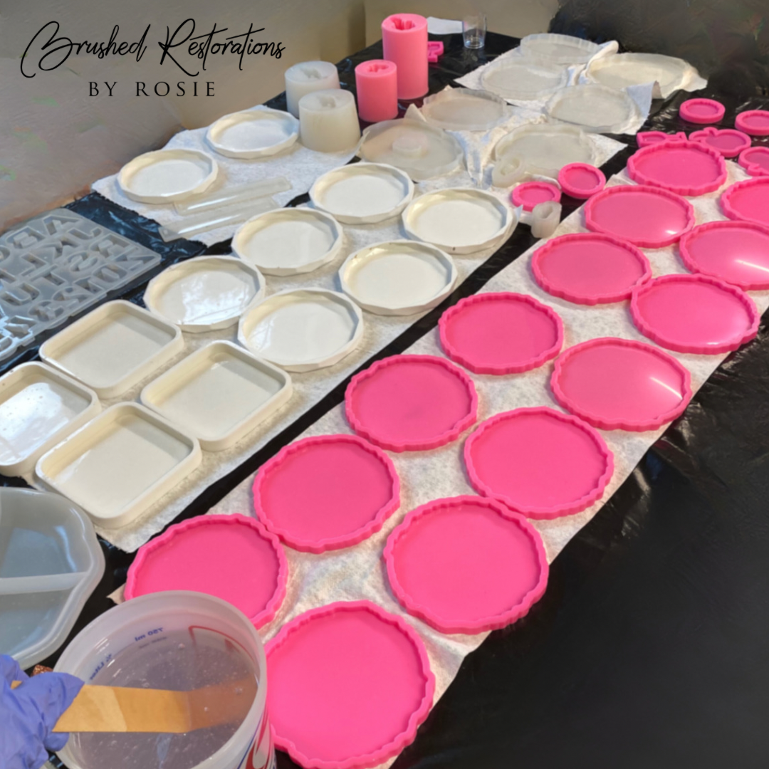 Variety of custom silicone resin molds in pink and white for crafting coasters, trays, and decorative pieces by Brushed Restorations