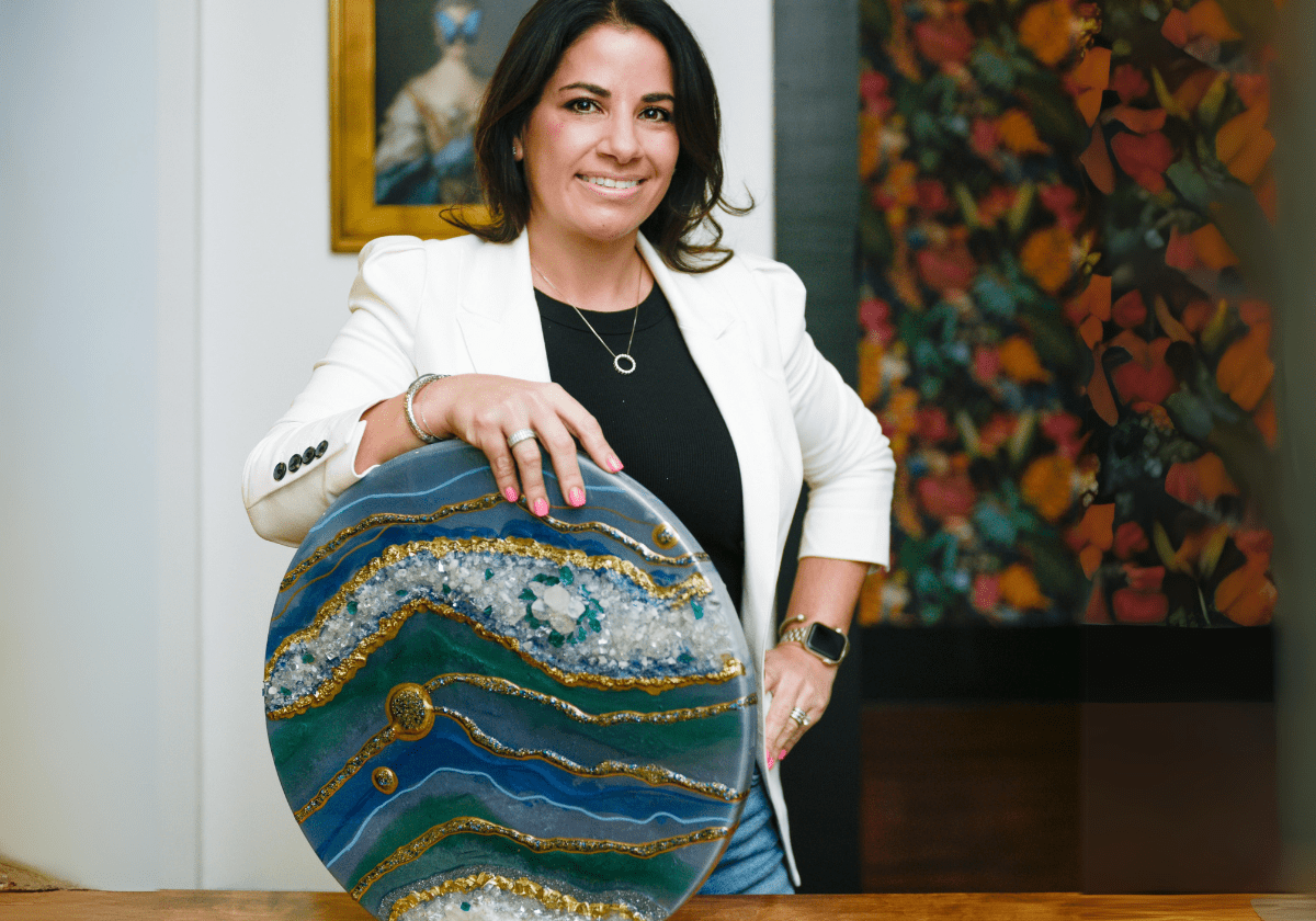 Smiling artist in a white blazer showcasing an exquisite geode resin art piece, symbolizing the blend of creativity and business acumen in resin artistry